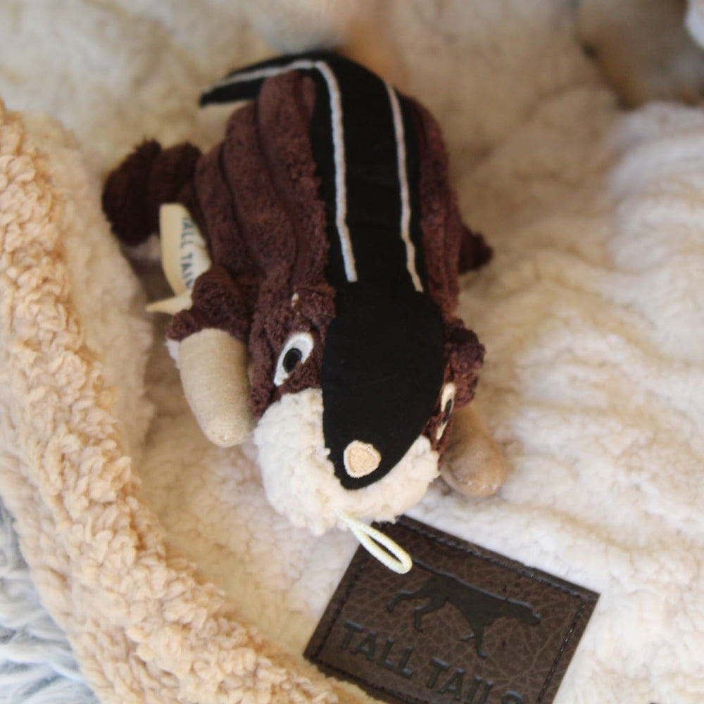 A dog cuddling the Tall Tails Chipmunk plush squeaker toy.